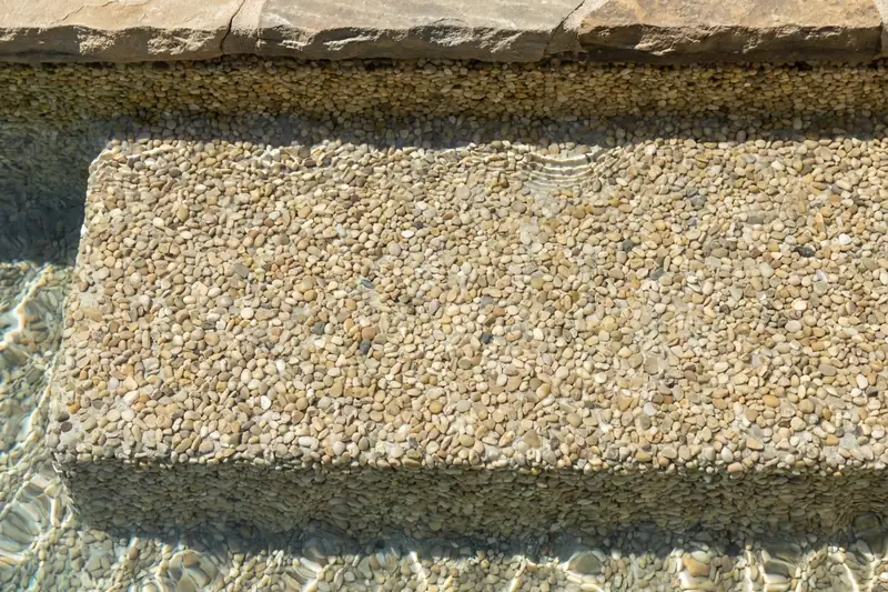 Close view of a sand-colored pebble finish on a pool step