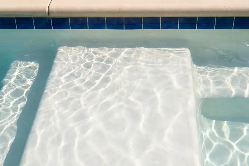 Close view of a smooth white plaster pool step under clear water